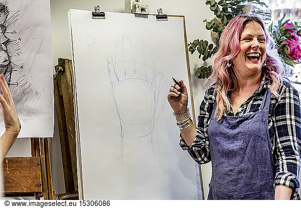 Lachende Frau mit Schürze  an einer Staffelei stehend  Zeichnung einer menschlichen Hand.