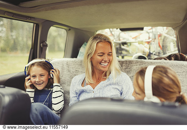 Lachende Mutter und Töchter mit Kopfhörer auf dem Rücksitz des Autos