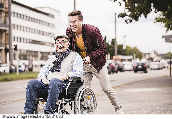 Lachender junger Mann schiebt glücklichen älteren Mann im Rollstuhl