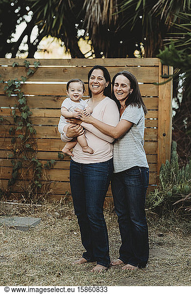Lachendes Baby mit zwei Zähnen im Hinterhof mit zwei barfüssigen Müttern