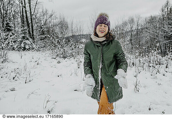 Lachendes jugendliches Mädchen  das Schnee hält  während es im Winter im Schnee steht