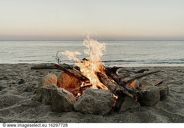 Lagerfeuer am leeren Strand bei Sonnenuntergang
