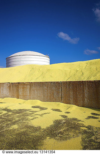 Lagertank durch Sandhaufen in der Fabrik gegen blauen Himmel