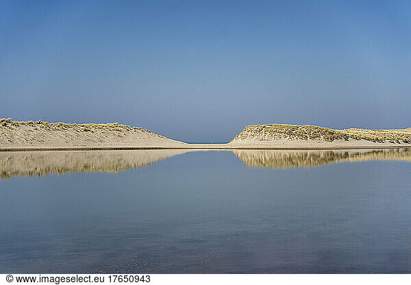 Lagoon with sand dunes under clear sky