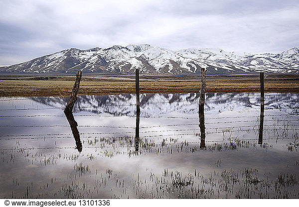lake surrounded by fencing by snowcapped mountain against cloudy sky