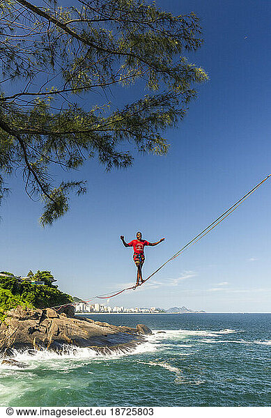 Landscape of man walking on highline over ocean on rocky shore