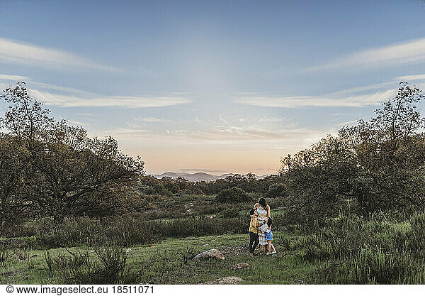 Landscape of young mother and children hugging under blue sky in field