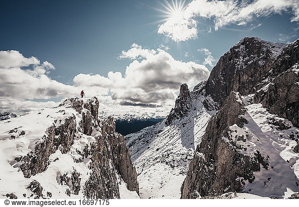 Landschaftsaufnahme einer Bergsteigerin auf einem Gipfel vor blauem Himmel