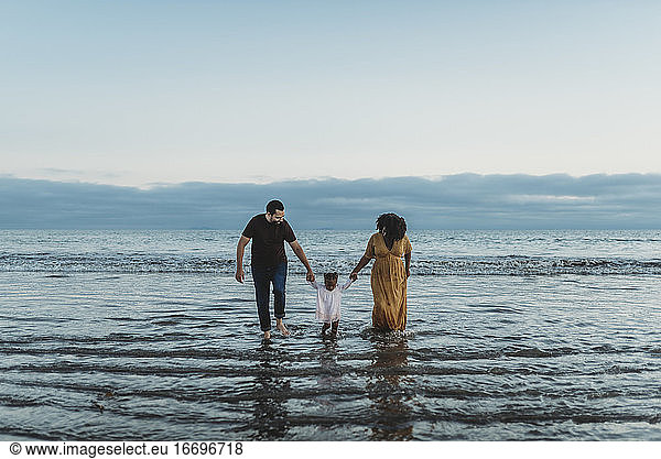 Landschaftsaufnahme einer jungen dreiköpfigen Familie  die gemeinsam im Meer spazieren geht