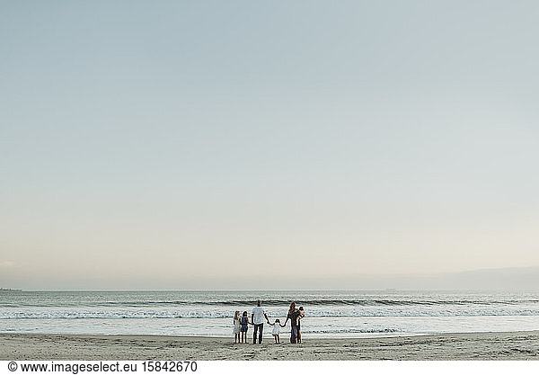 Landschaftsaufnahme einer jungen Familie  die bei Sonnenuntergang im Meer steht