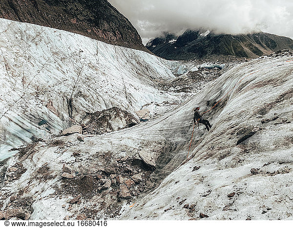 Landschaftsaufnahme eines Bergsteigers beim Abseilen auf einem Gletscher bei bewölktem Himmel