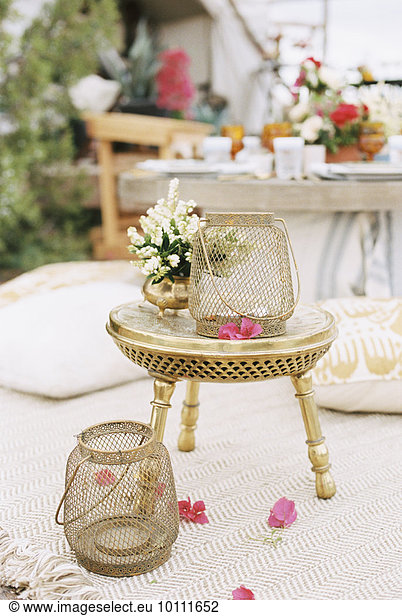 Lanterns and flowers on a small brass table outside a tent in a desert.