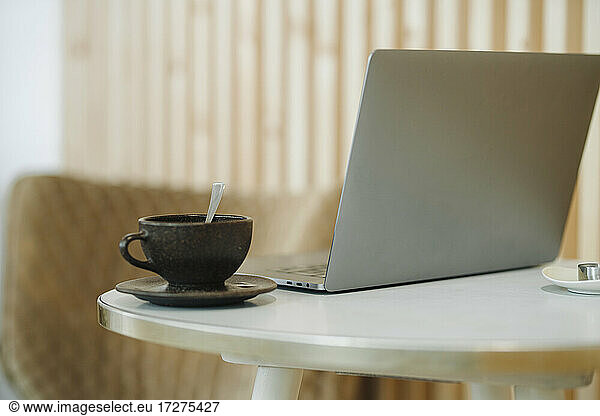 Laptop and coffee cup kept on table in cafe