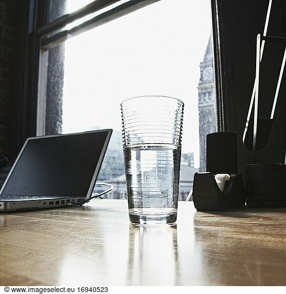 Laptop and drinking water glass on desk in urban office.