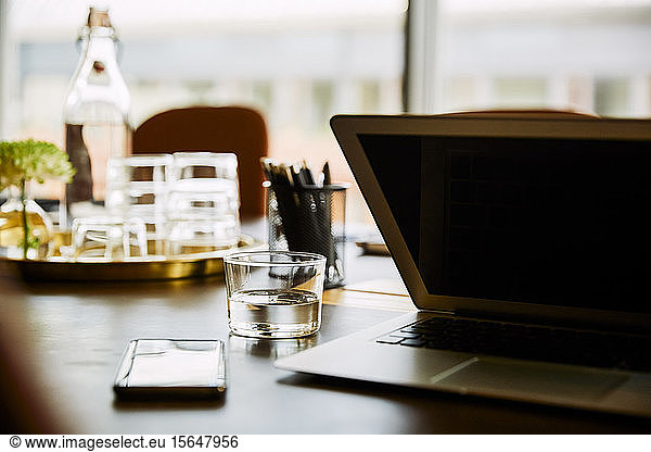 Laptop by drinking glass on conference table in board room