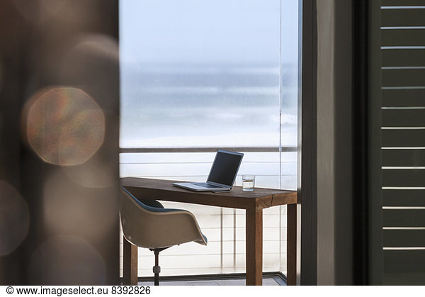 Laptop on desk in modern home office overlooking ocean