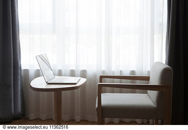 Laptop on desk with chair  in front of window