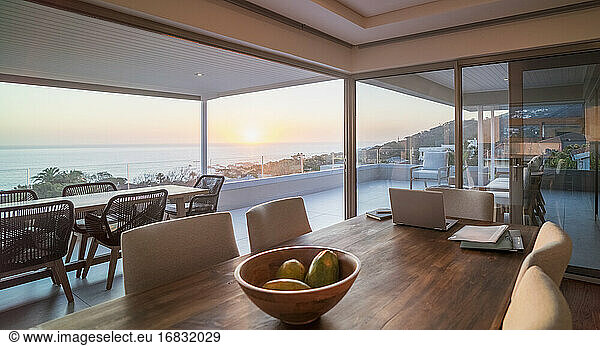 Laptop on luxury dining table with scenic ocean view at sunset