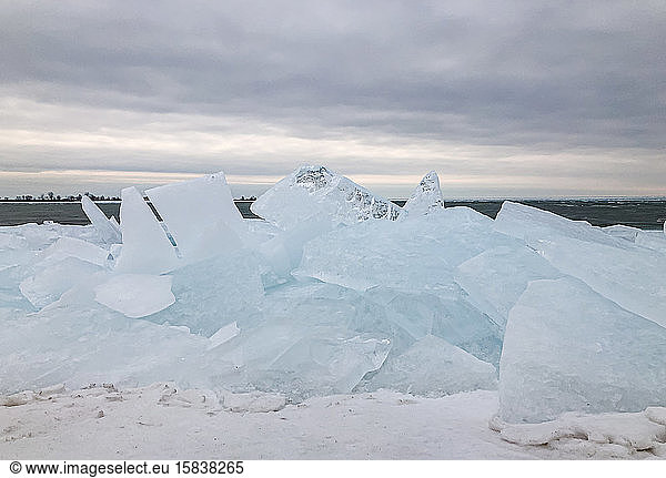 Large flat pieces of ice piled up along the shore of a lake in winter.