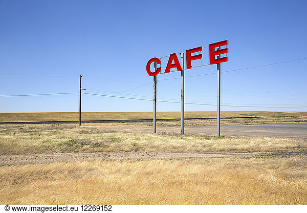 Large red capital letters on metal poles advertising cafe in a prairie.
