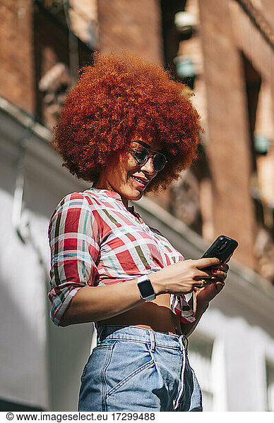 Lateinamerikanische Frau mit Afro-Haar  die ein Mobiltelefon benutzt