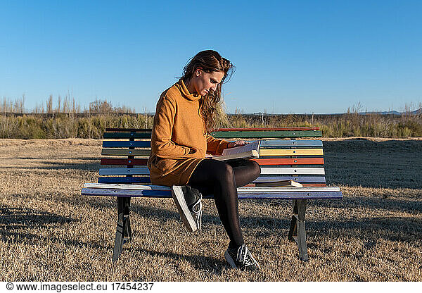 Latin girl reading book on multicolored bench