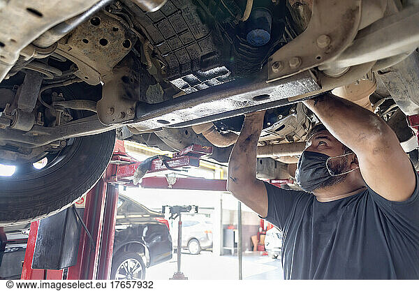 Latin male mechanic working beneath a malfunctioning dirty automobile