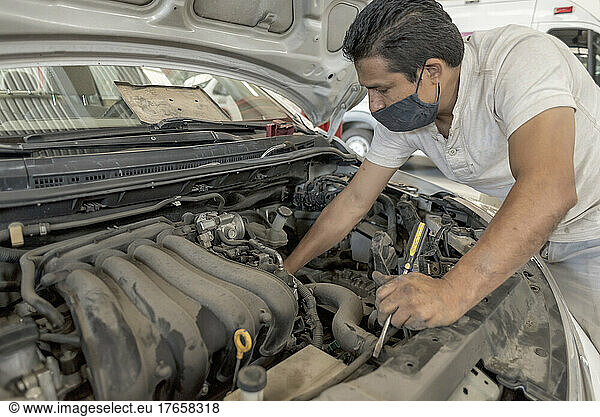 Latin male mechanic working on a malfunctioning dirty automobile