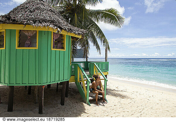 Latin man  chilling on staircase of colorful beach hut during holidays