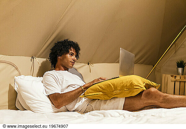 latin man waving in a video call lying on the bed in a tent