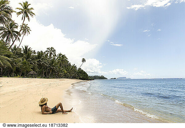Latin man  wearing straw hat  tanning on golden sandy beach  Samoa