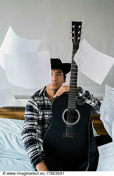 Latin man with guitar on bed with note sheets floating around