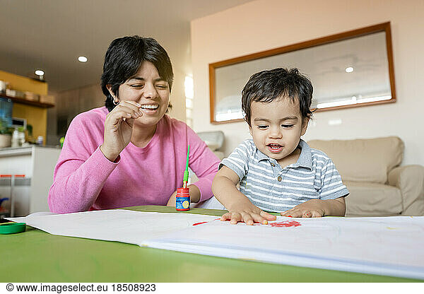 Latin mother and little son painting together hand using tempera