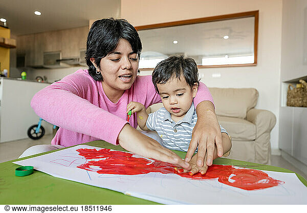 Latin mother and little son painting together hand using tempera