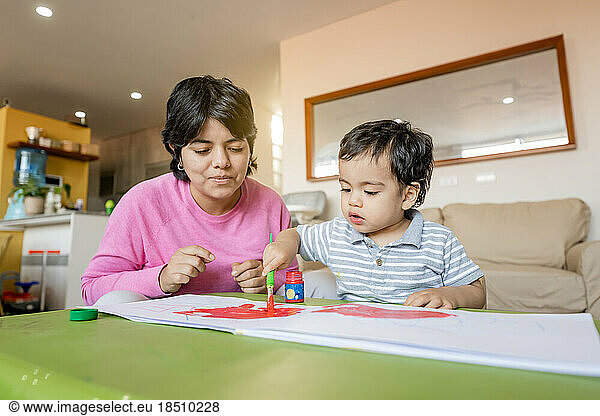 Latin mother and little son painting together with tempera colors.