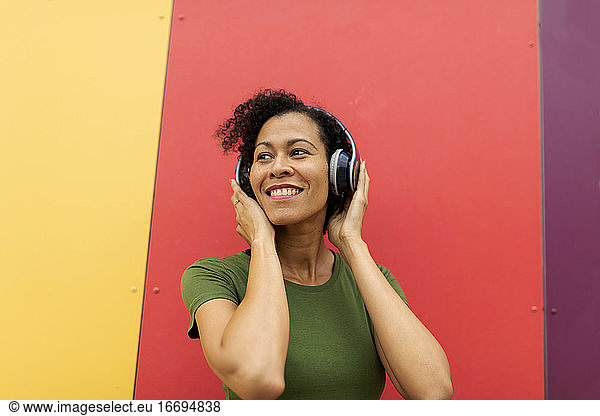 Latin woman wearing headphone listen to music against colorful wall