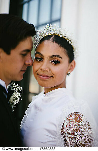 Latina bride makes eye contact while husband snuggles her