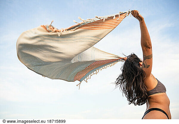 Latina woman having fun at the beach with towel in the wind