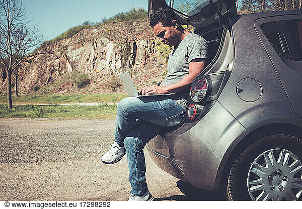 latino man searching on laptop for help sitting in back of car