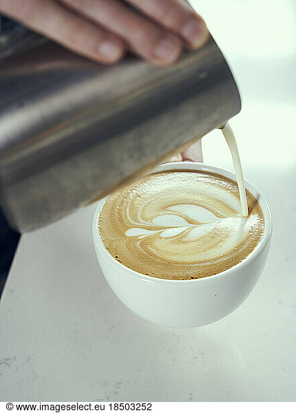 Latte art being hand poured into a fresh latte in a white mug.