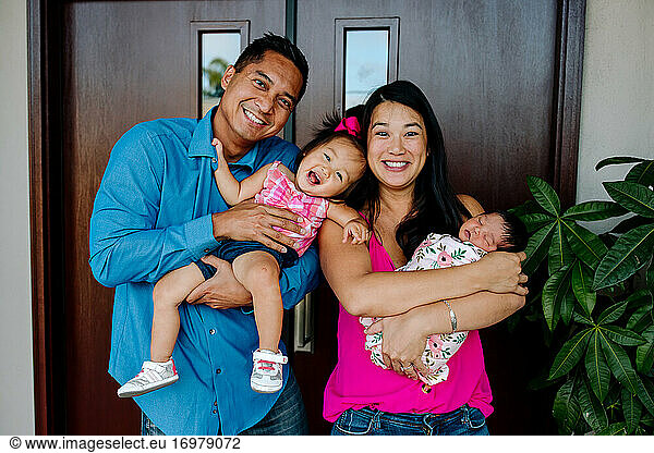 Laughing Asian-American family with newborn and year-old daughter
