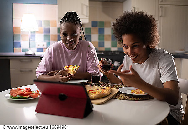 Laughing ladies having online call while dining at evening