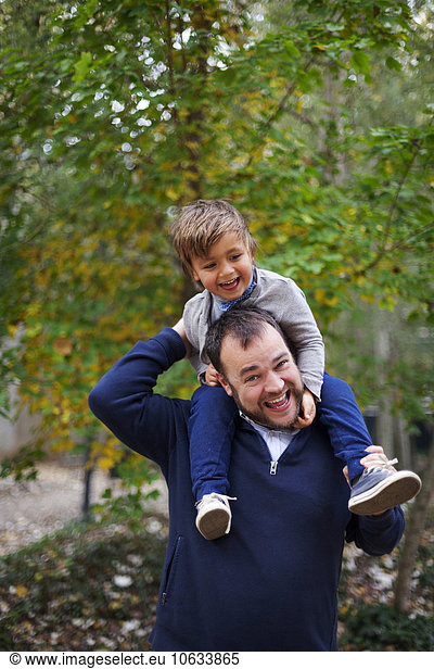 Laughing little boy sitting on his father's shoulders