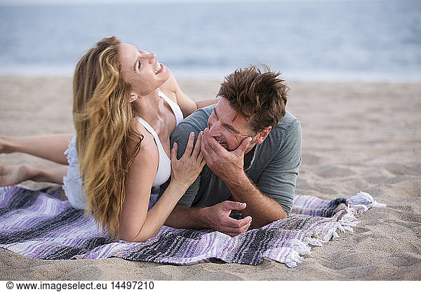 Laughing Mid-Adult Couple Laying on Blanket at Beach