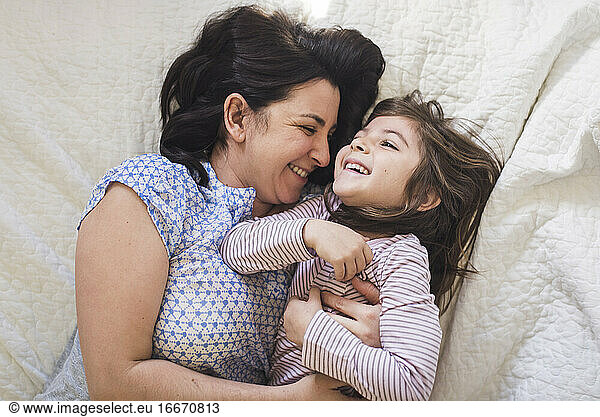 Laughing mom and 6 yr old daughter snuggling in bed