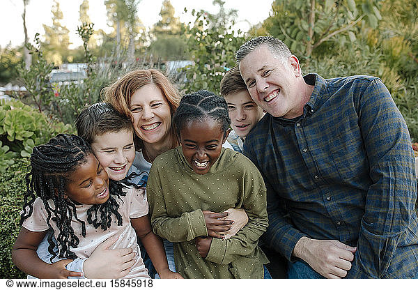 Laughing multiracial family hugging outdoors surrounded by plants