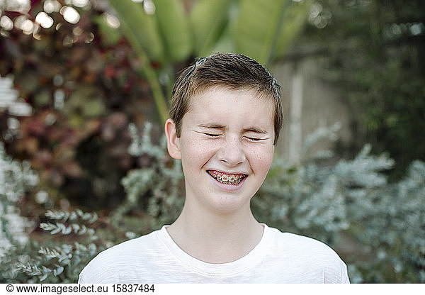 Laughing preteen boy with short hair and braces near lush plants