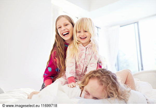 Laughing sisters on top of father on bed