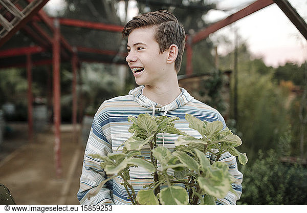 Laughing teen boy with braces and short hair holding landscape plant
