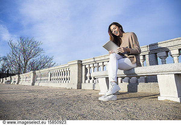 Laughing woman using her tablet while seated on a bench